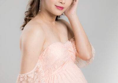 A pregnant woman in a pink dress posing for a photo.