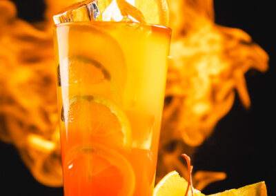 A cocktail with orange slices and cherries in front of flames.