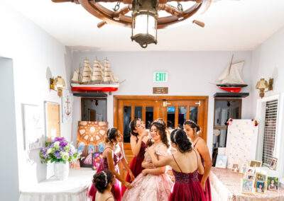 A bride and her bridesmaids posing in front of a ship wheel.