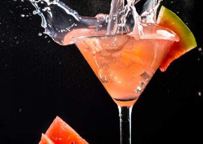 A watermelon martini being poured into a glass on a black background.