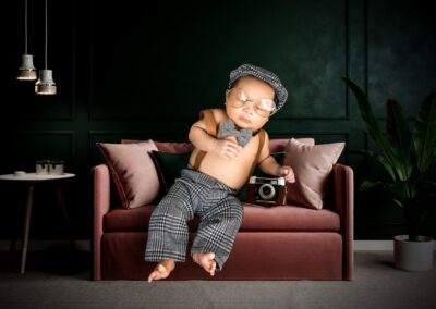 A baby sitting on a couch with a camera.