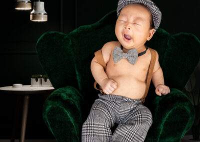 A baby is sitting in a green chair with a bow tie.