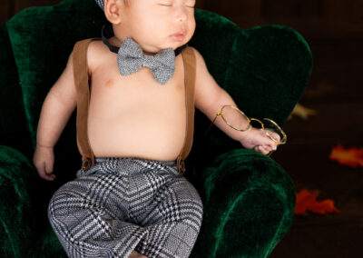 A baby boy wearing a hat and bowtie in a green chair.