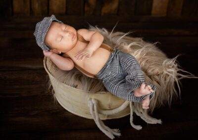 A baby boy is laying in a basket with a hat on.