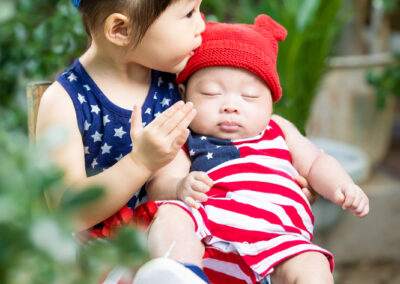 A baby in an american flag outfit kissing a baby in a red, white and blue outfit.