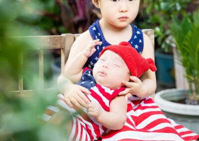 A little girl is sitting on a wooden bench holding a baby.