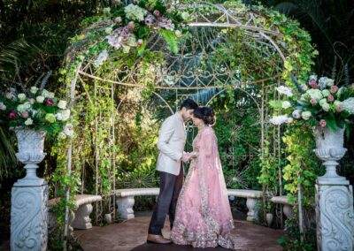 A bride and groom kissing under an archway in a garden.