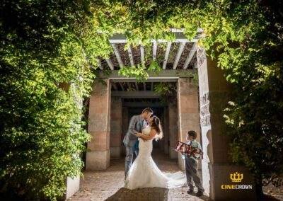CineCrown Photo A bride and groom kissing under an archway in a garden.