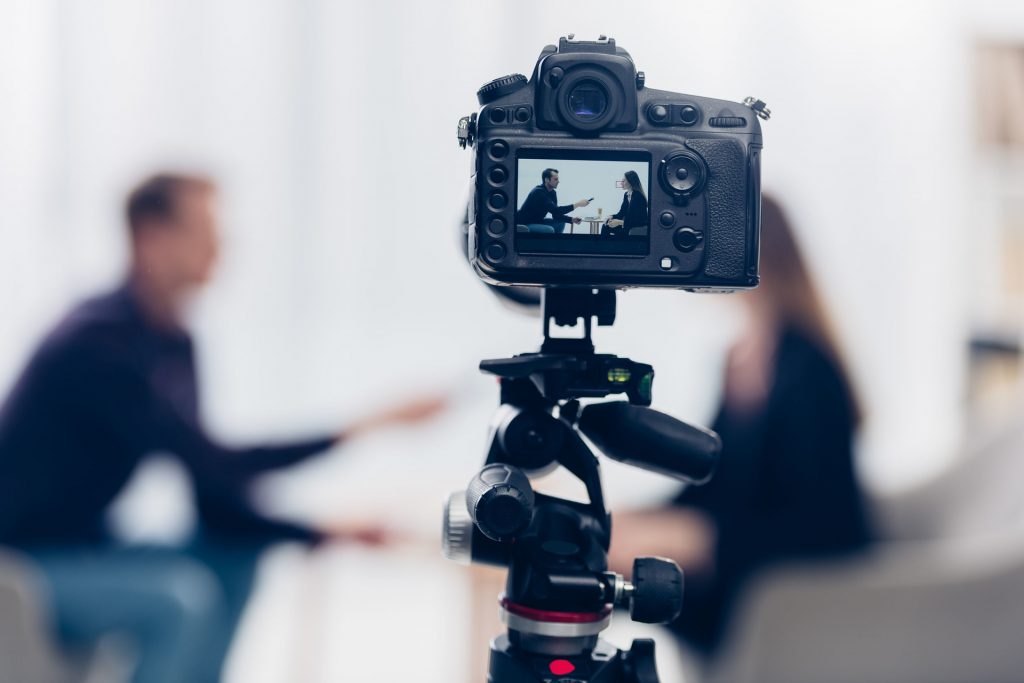 businesswoman in suit giving interview to journalist in office, camera on foreground