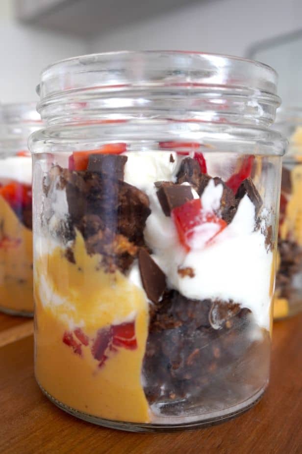 Frasco de desayuno saludable con capas de yogur griego, fresas, mantequilla de maní y avena al horno sabor brownie.