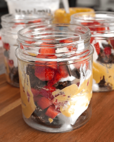 Frascos de desayuno alto en proteína con yogur griego, fresas y avena al horno sabor brownie.