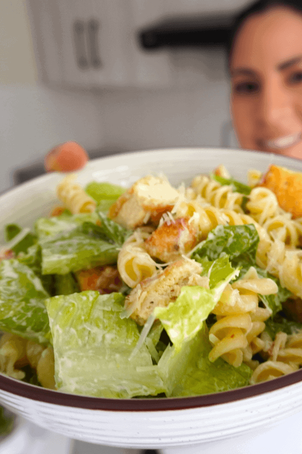 Ensalada César con pasta alta en proteína preparada con pollo, lechuga romana, queso parmesano y aliño cremoso.