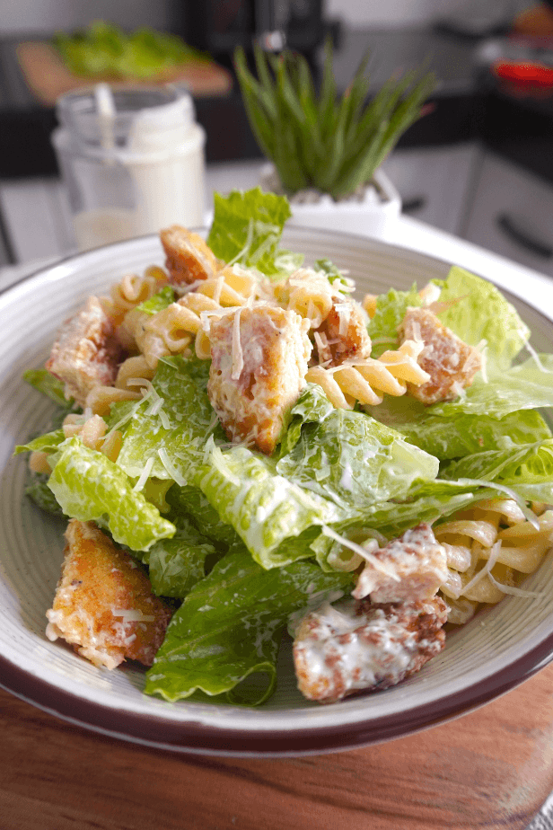 Mezclando pasta, pollo, lechuga romana, queso parmesano y aliño César casero.