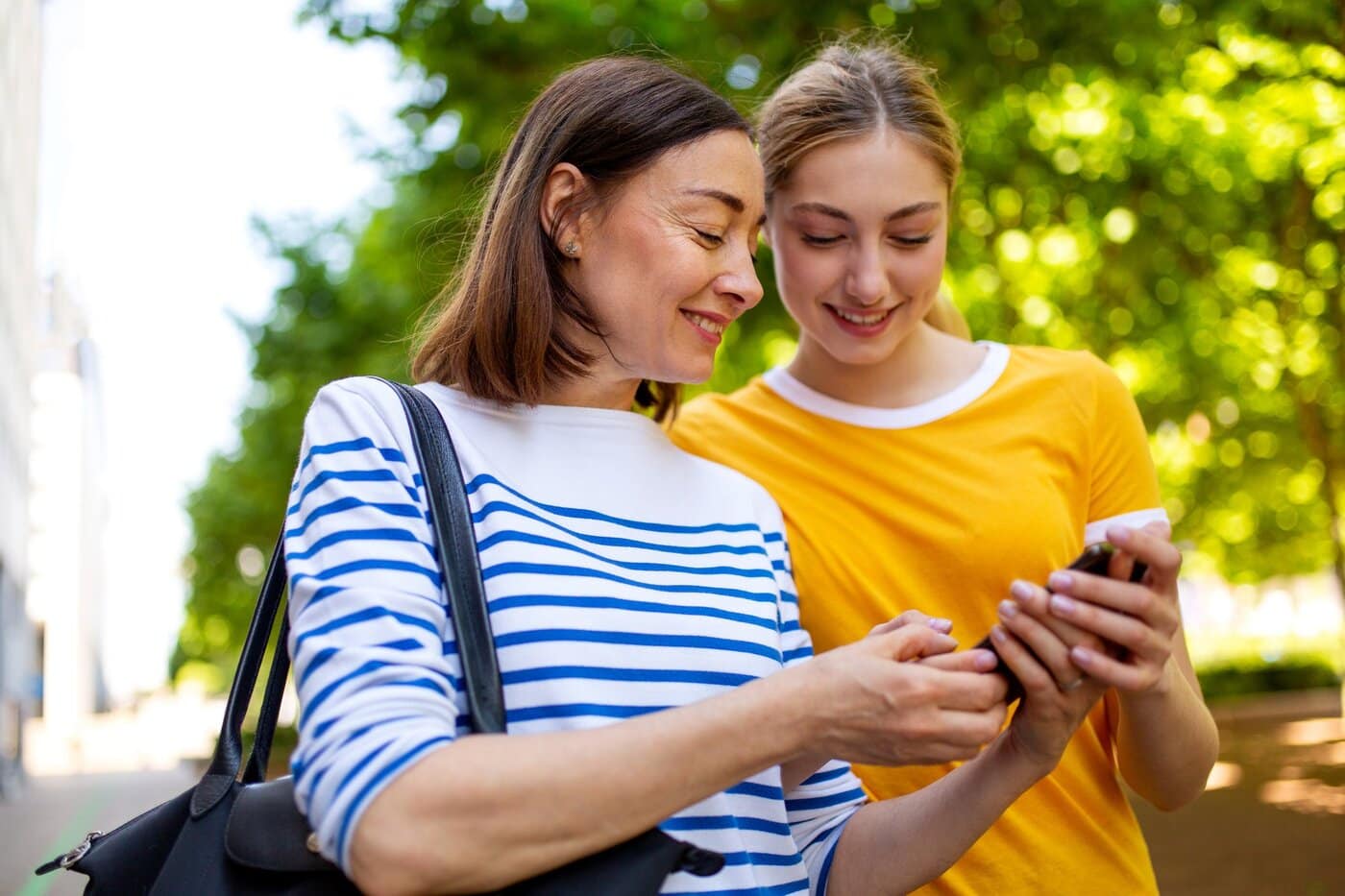 Portrait of smiling mother and daughter looking art cellphone in park