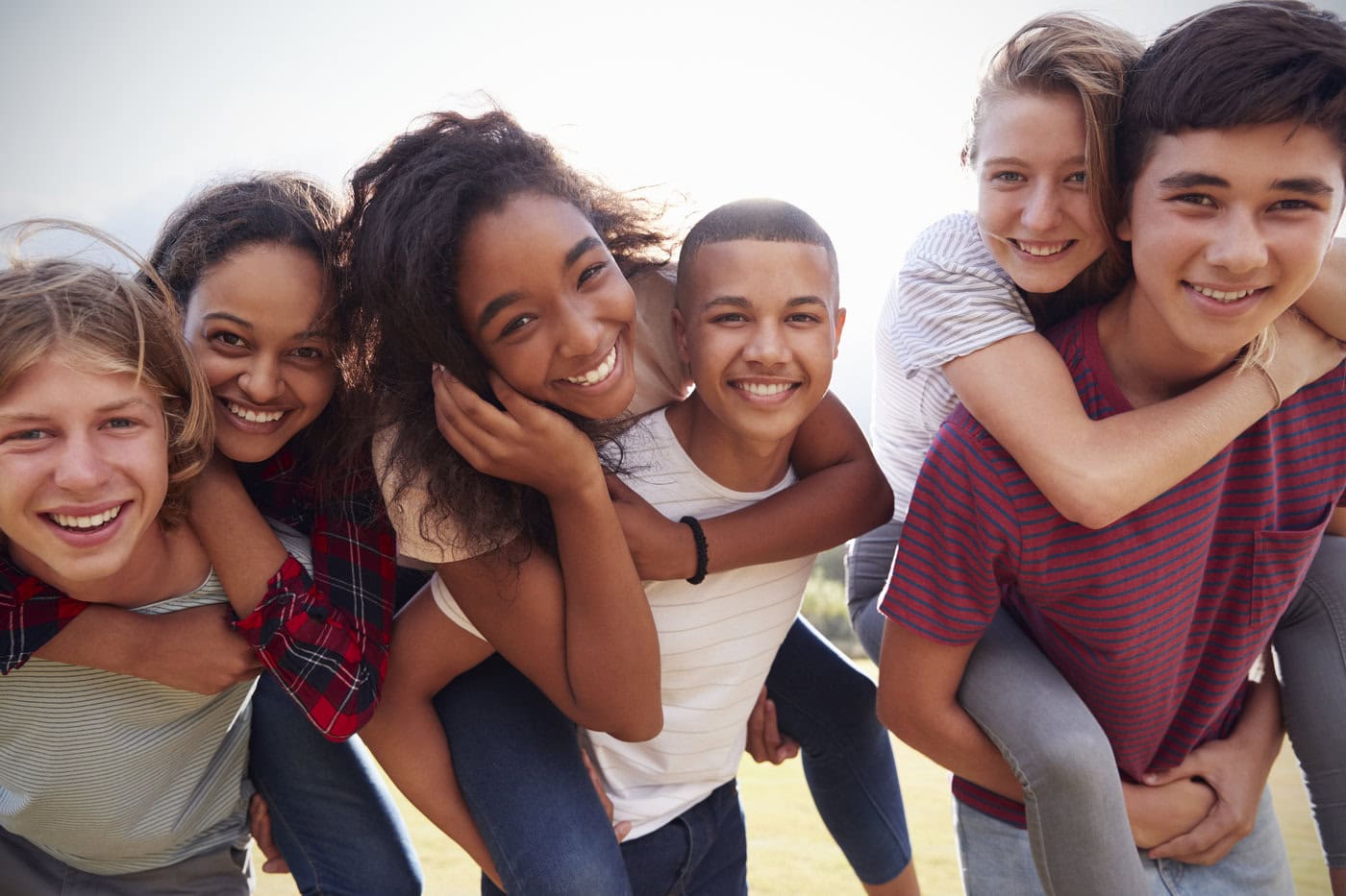 Image of teenage school friends having fun piggybacking outdoors