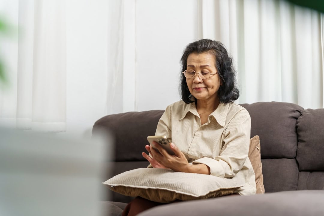 Image of an older woman sitting on the couch looking at her phone.