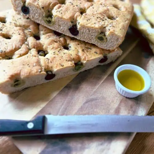 Olive and rosemary focaccia on a chopping board with a pot of oil