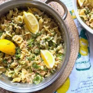 salmon and dill pasta in a pan with yellow lemon wedges
