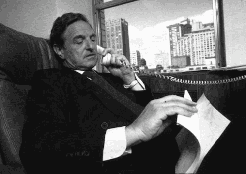 Warren Buffett reading a document in his office with city skyline view.
