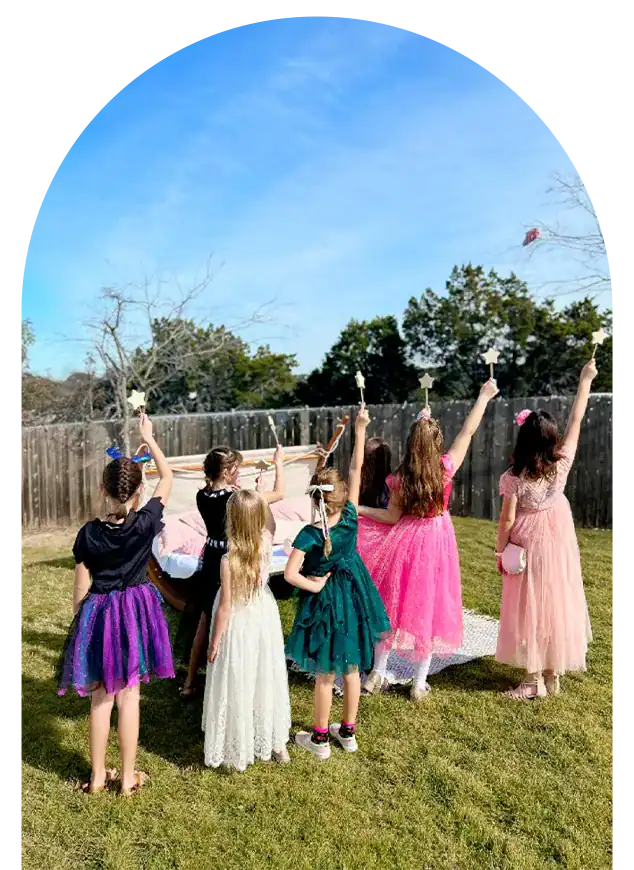 Girls in vibrant dresses raising hands outdoors during event.