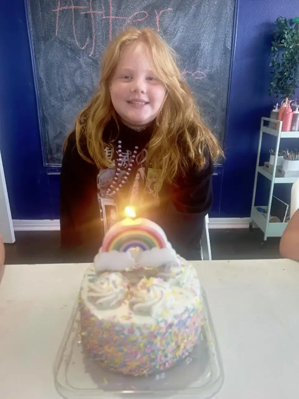Happy girl with rainbow cake and candle at after school celebration.