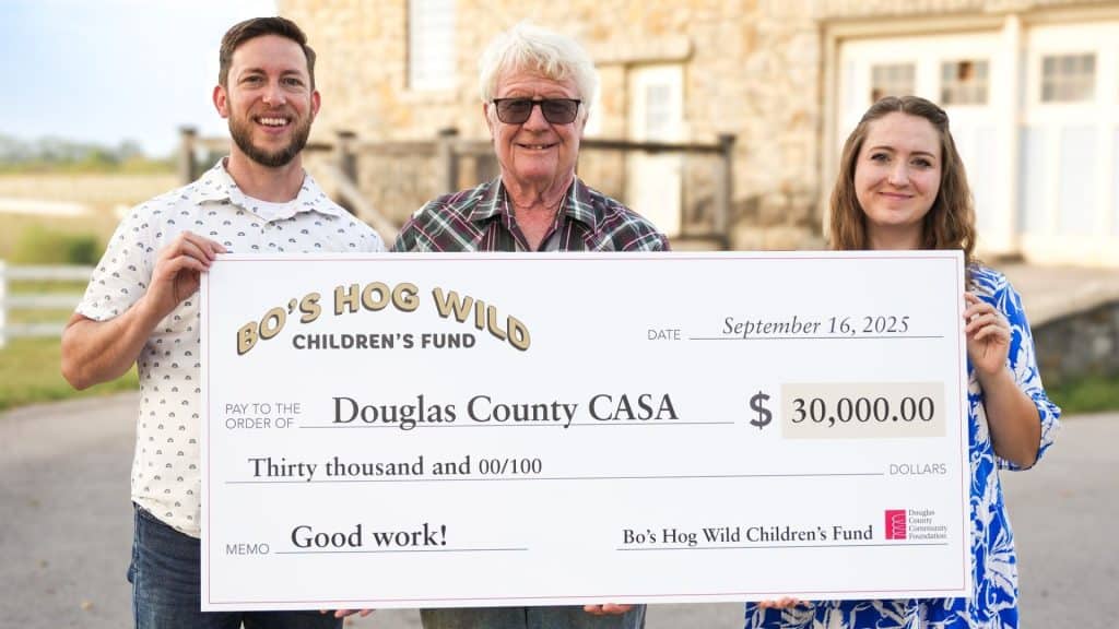 $ALT: Three people holding a large donation check for Douglas County CASA, celebrating charitable donation for children's support, outdoors in front of a stone building.