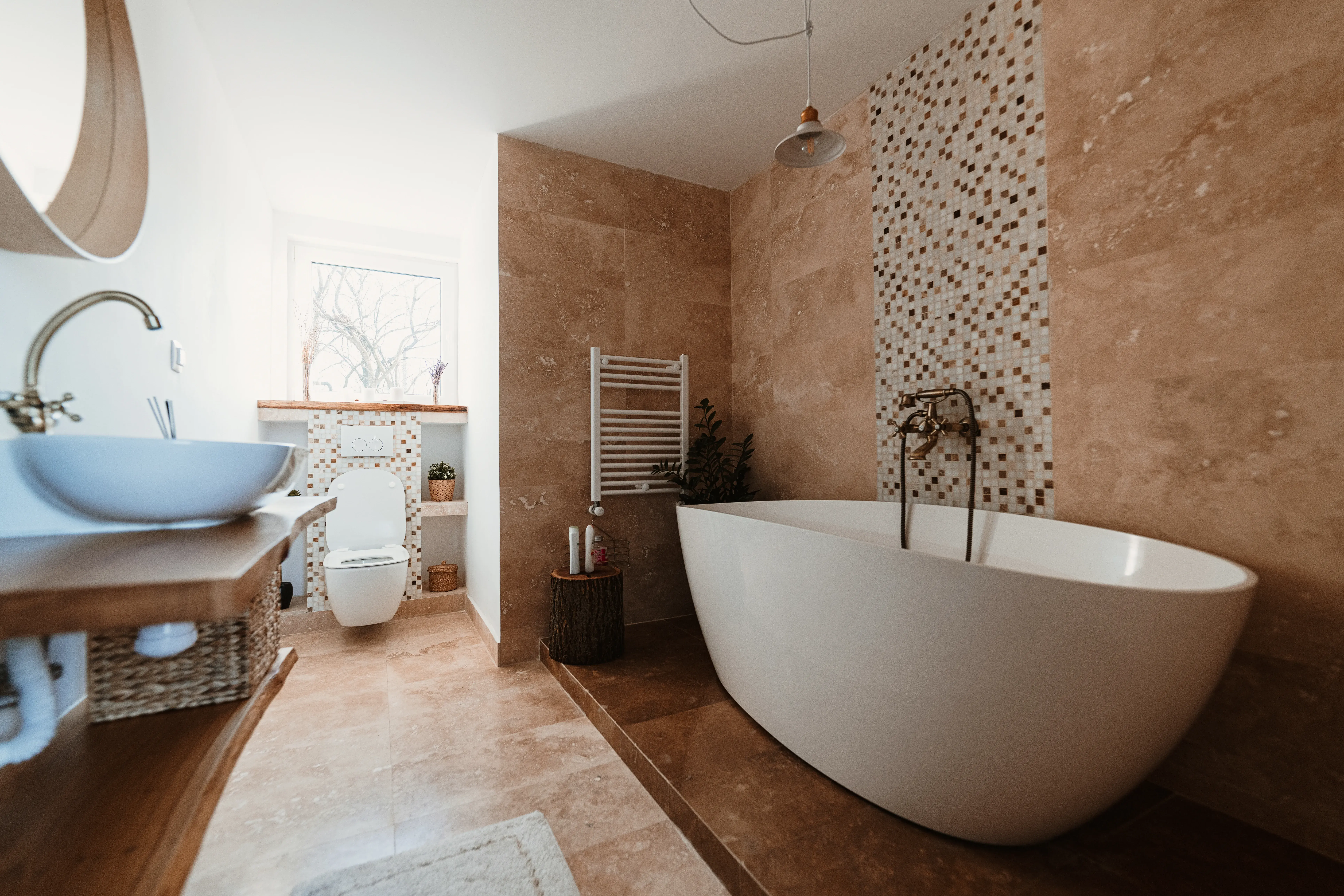 Modern freestanding bathtub in a stylish bathroom with earthy tones and mosaic tile accent wall.