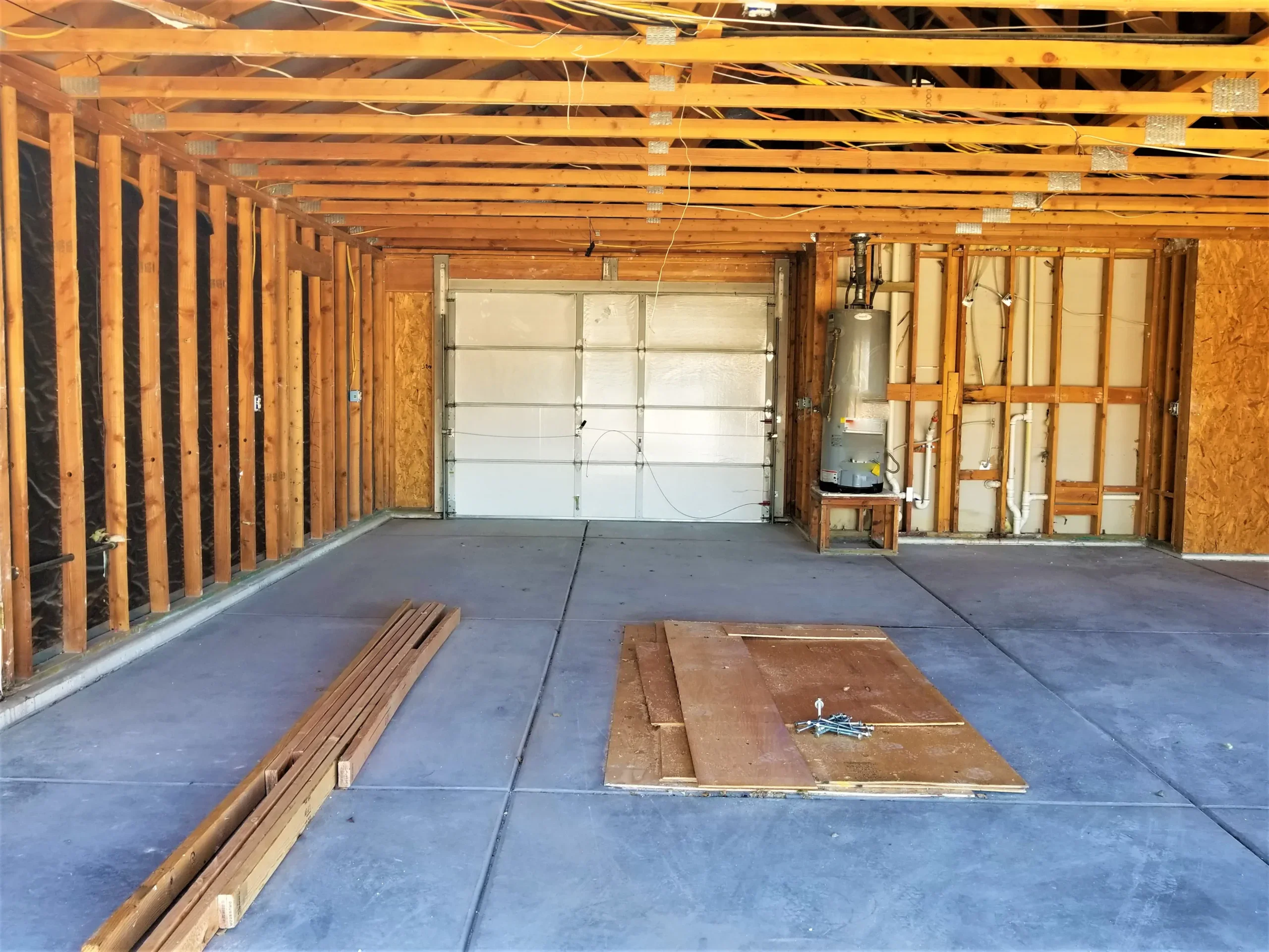 Garage interior under construction with exposed wooden framing and concrete floor.