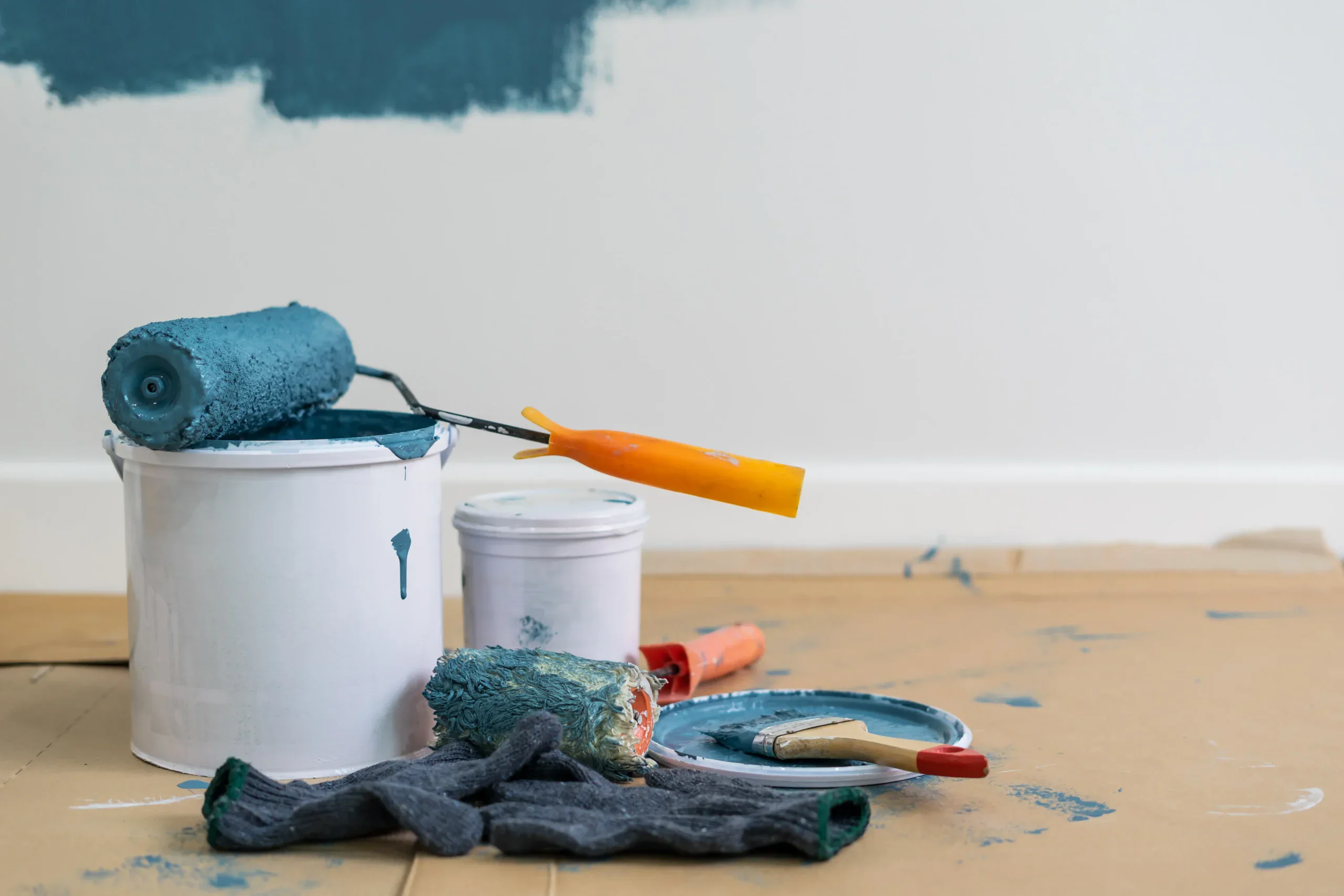 Paint can, roller, brush, and supplies on drop cloth during room renovation.