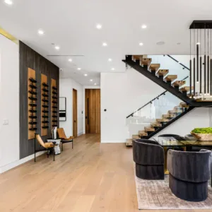 Modern living room with wooden floors, glass staircase, and wine rack.