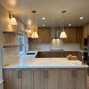 Modern kitchen with light wood cabinets, white countertops, and pendant lights.
