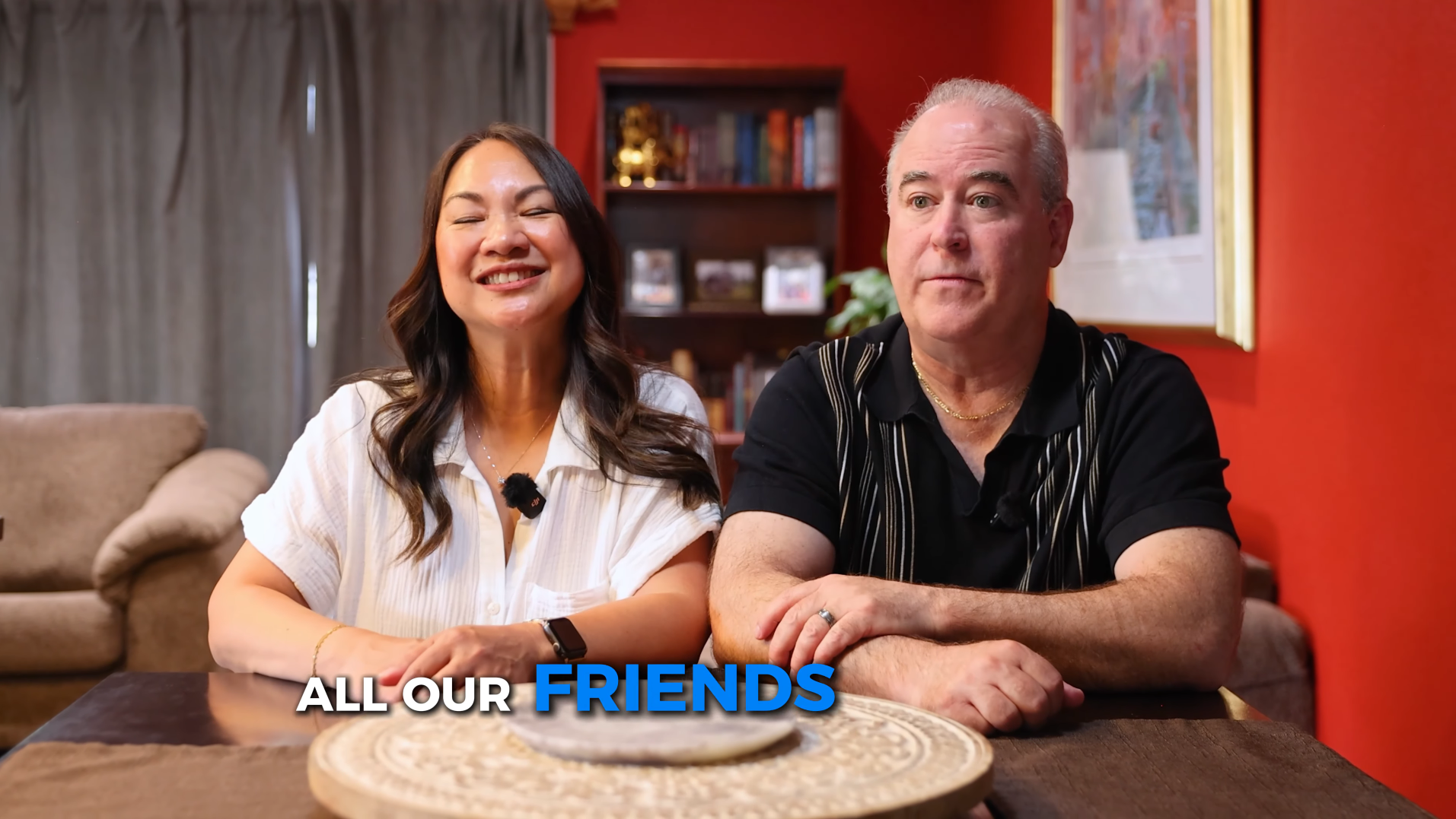 Two friends smiling at a table in a cozy living room setting.