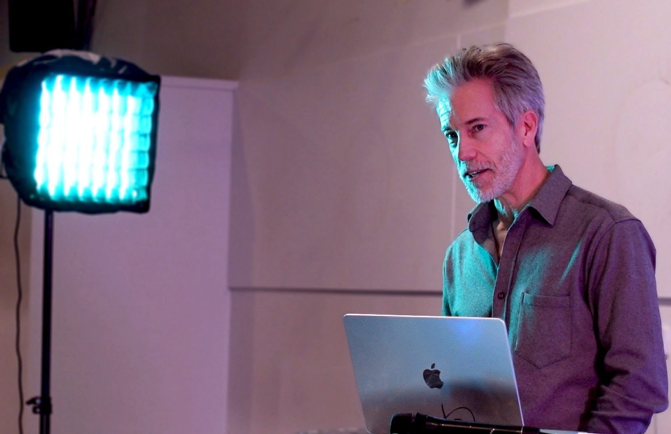 Close-up profile of Dave Gougé behind his laptop speaking under direct stage lighting at the Gold Coast Hub Production and Pints media event.