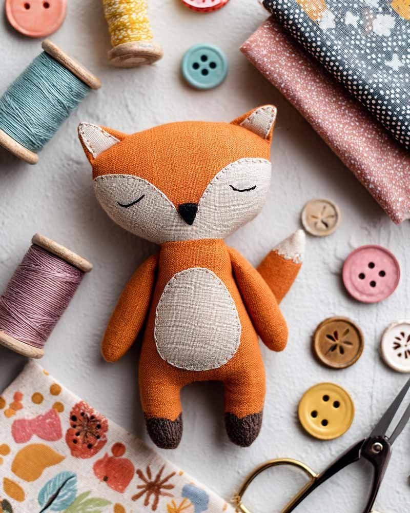Handmade orange fabric fox toy with sewing patterns, colorful threads and craft tools arranged neatly