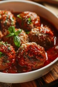 Juicy baked meatballs in marinara sauce topped with fresh basil and Parmesan, served in a white bowl — cozy homemade dinner recipe
