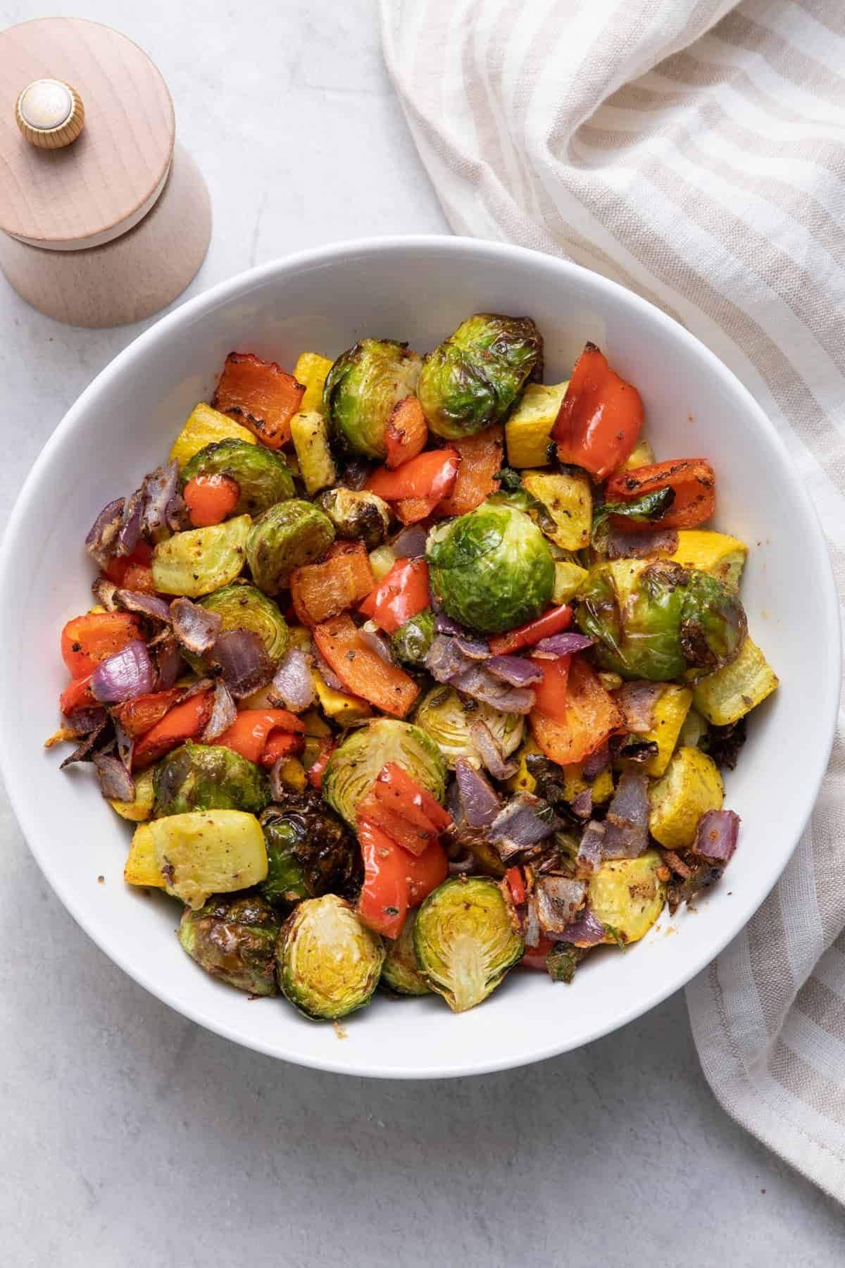 Bowl of air fryer vegetables including Brussels sprouts, bell peppers, squash, and onions.