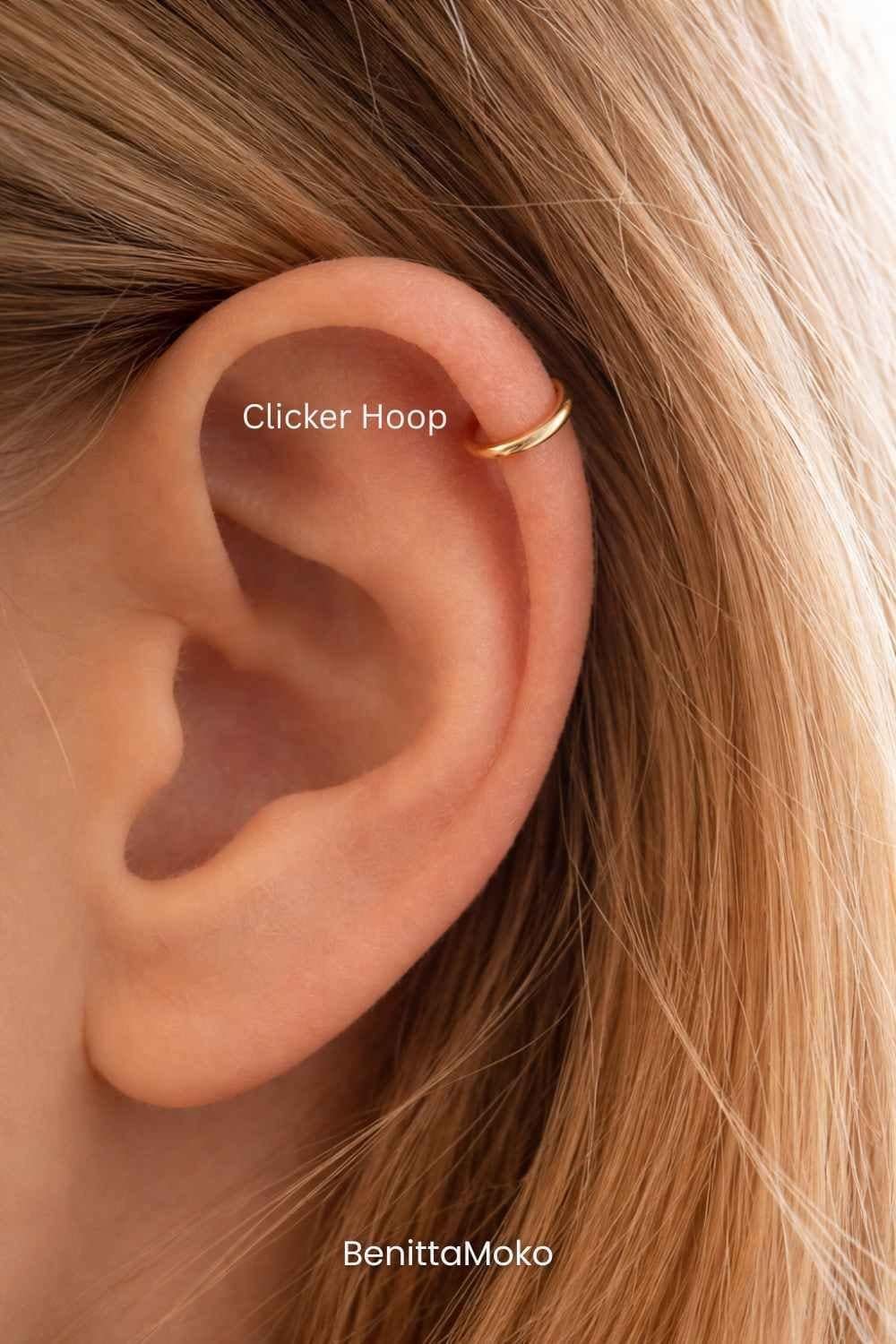 Thin gold clicker hoop in helix piercing, close-up of ear with minimalist cartilage jewelry in warm natural tones