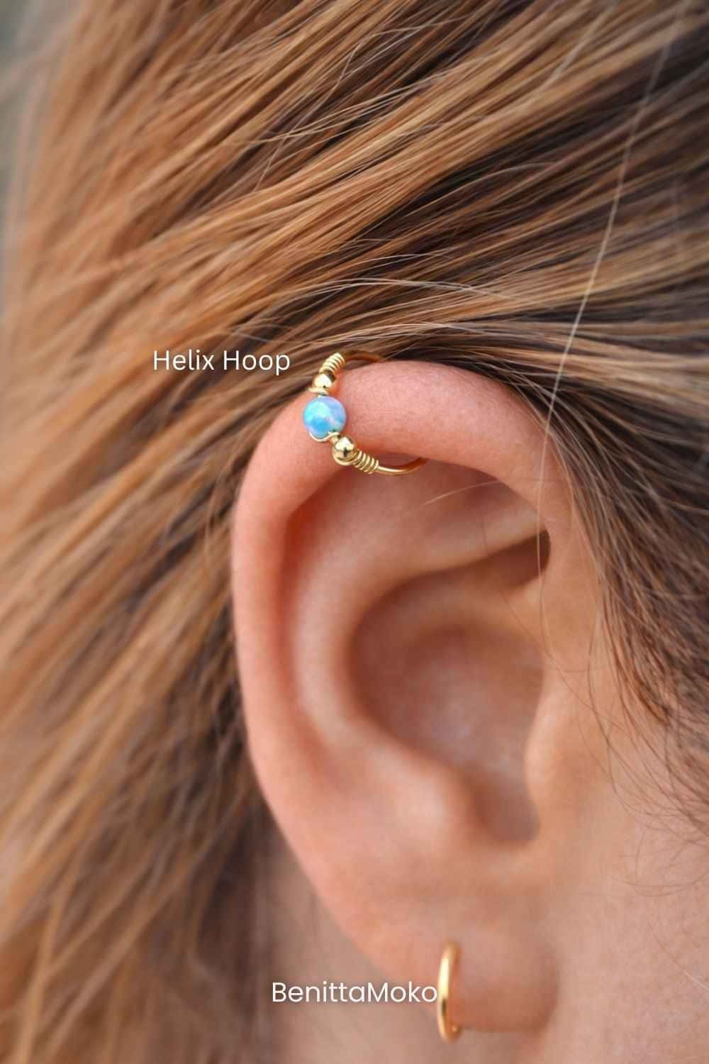 Gold helix hoop earring with blue opal bead worn on upper ear cartilage in a close-up view