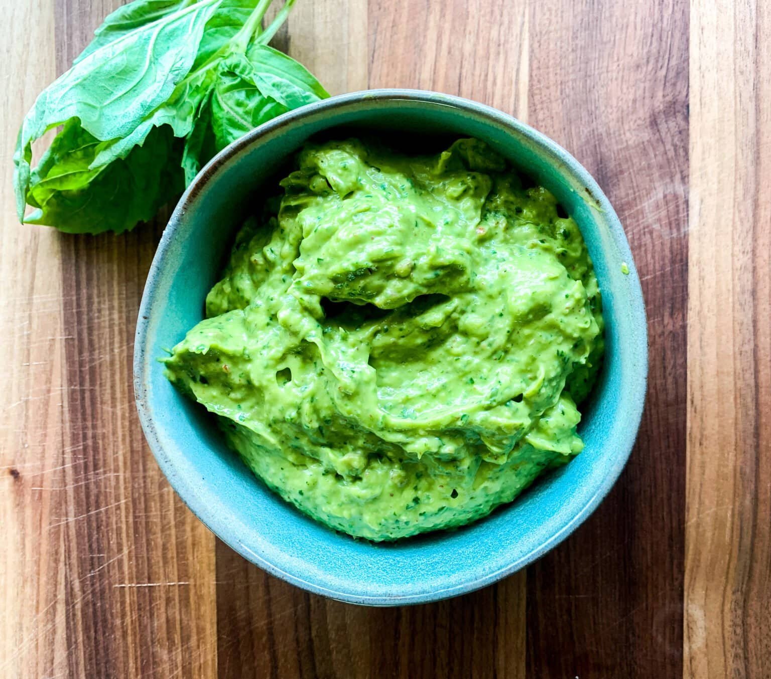 Homemade avocado pesto sauce in a bowl with fresh basil