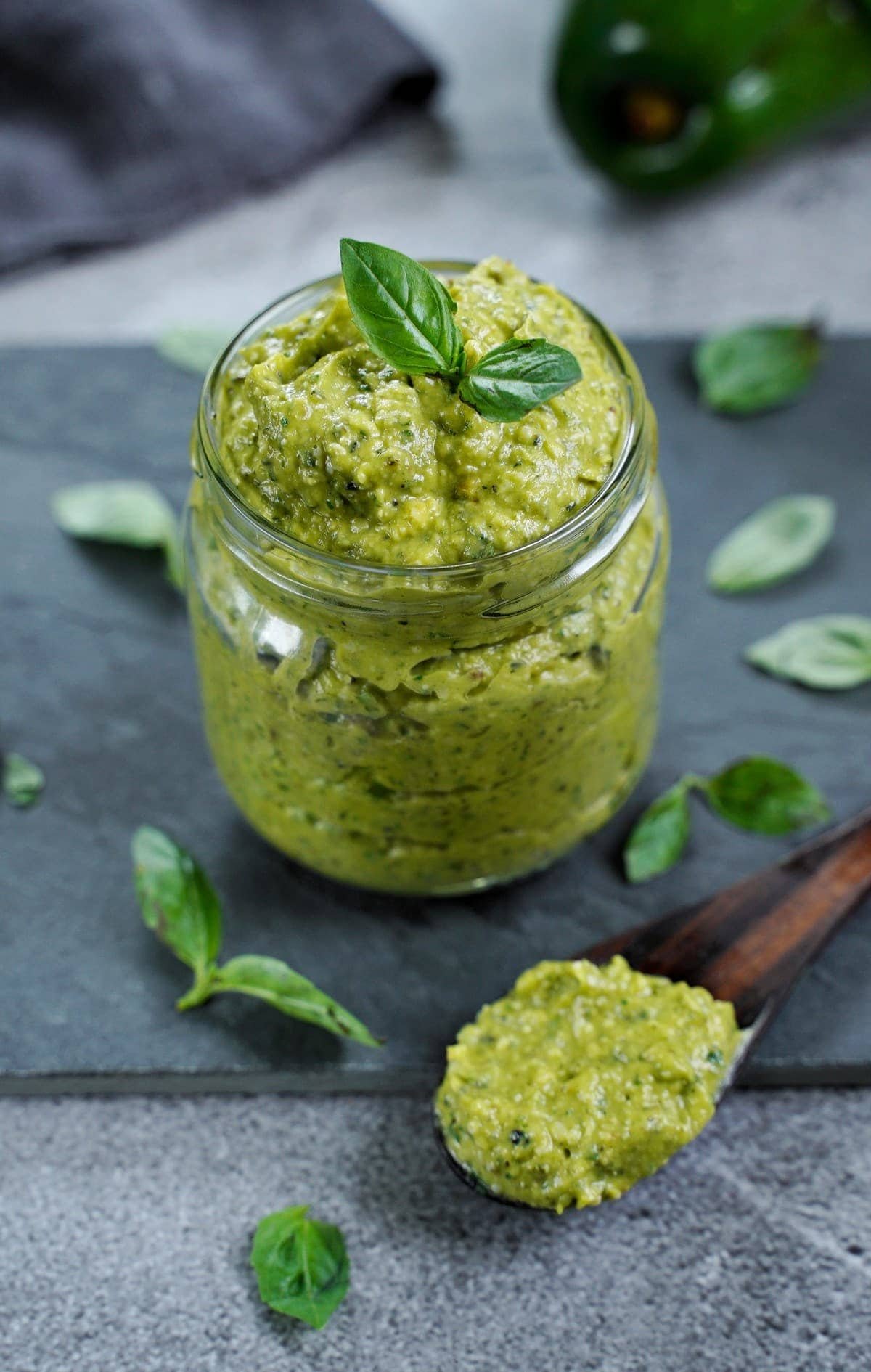 Nut-free avocado basil pesto in a glass jar with a wooden spoon