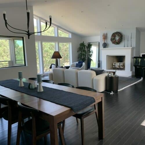 A modern, well-lit room with dark wood flooring, white sofas, a dining table, a fireplace, large windows, a chandelier, and a "JAZZ FESTIVAL" poster. A completed e-design interior design package by design-chat