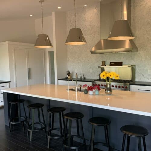 A modern kitchen interior with a white countertop island, black stools, stylish pendant lights, and a bouquet of yellow flowers for a pop of color.