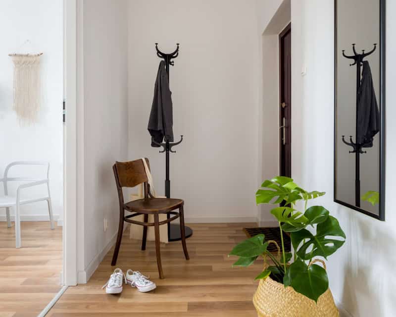A tidy hallway with wooden flooring featuring a coat stand, mirror, plant, a vintage chair, white shoes, and decorative wall art. A space perfect for an office nook e-design from design-chat.