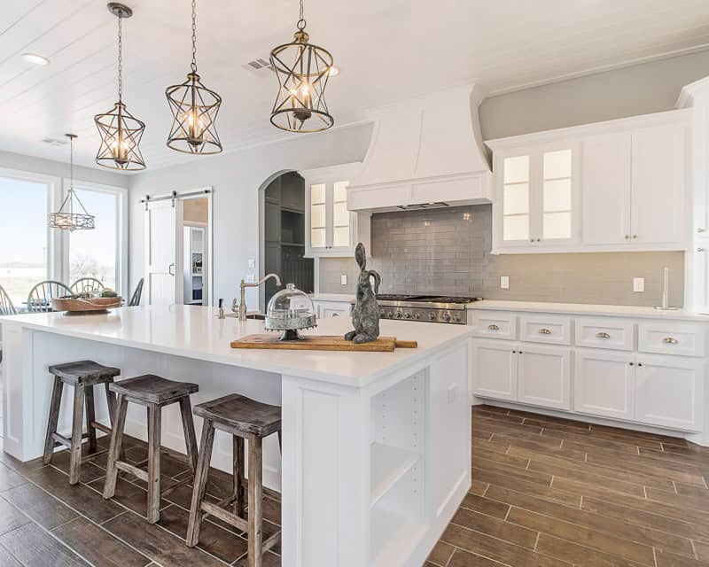 This image shows a bright, modern kitchen with white cabinets, a central island with stools, pendant lights, and stainless-steel appliances against subway tile backsplash. This room is perfect for e-design interior design by design-chat.