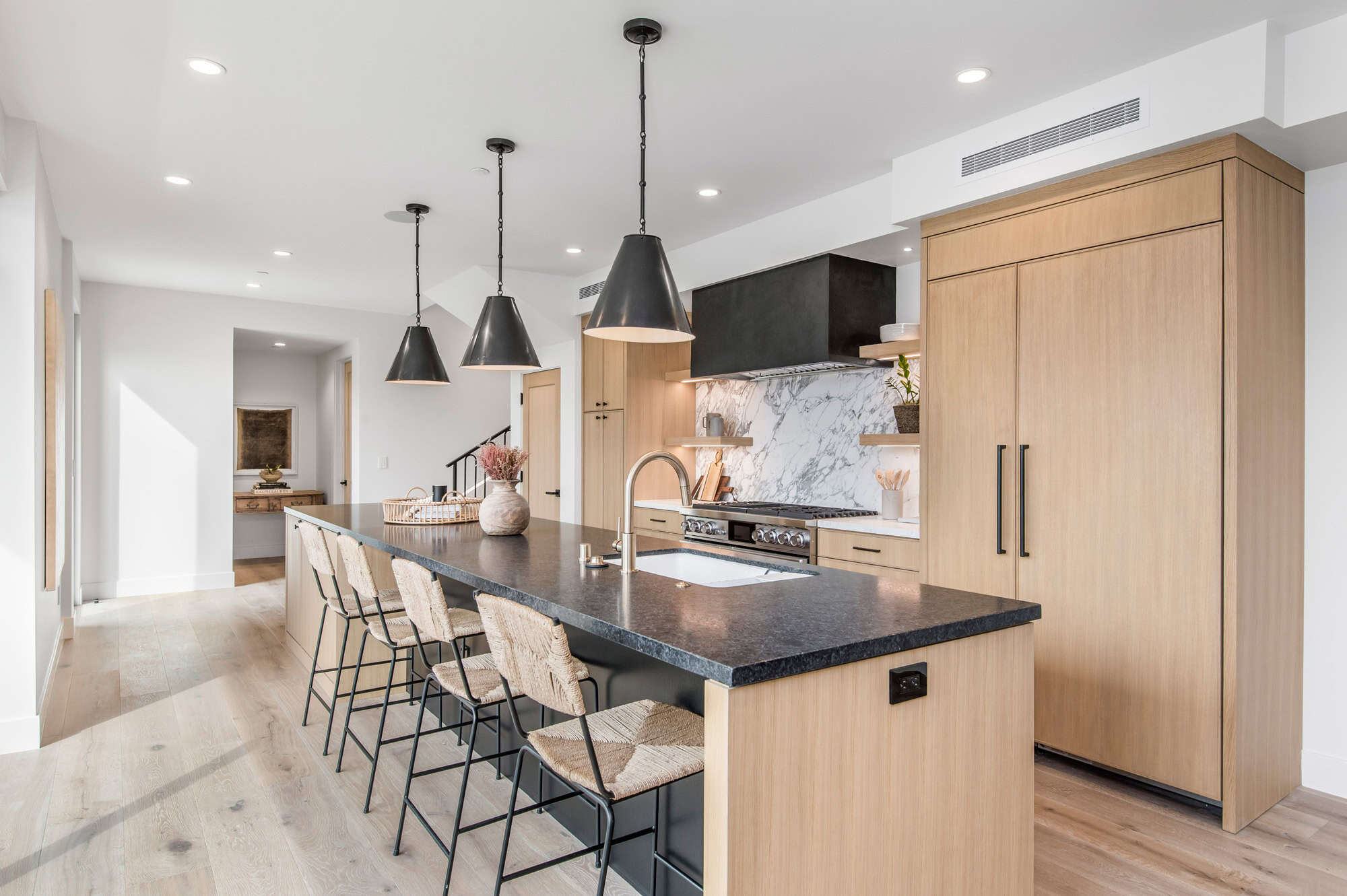 Scandinavian-inspired kitchen with light wood cabinetry, black countertops, waterfall island, and pendant lighting