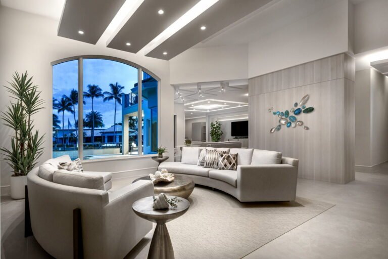 Elegant coastal living room at night with modern lighting, arched window, and curved white sectional