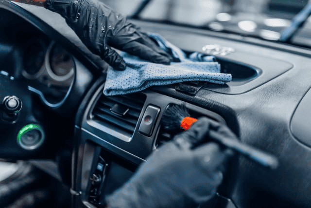 Interior Car Detailing Services in Saint James NY Close-up of hands in black gloves cleaning a car's dashboard with a cloth and brush during car detailing in Saint James, NY.