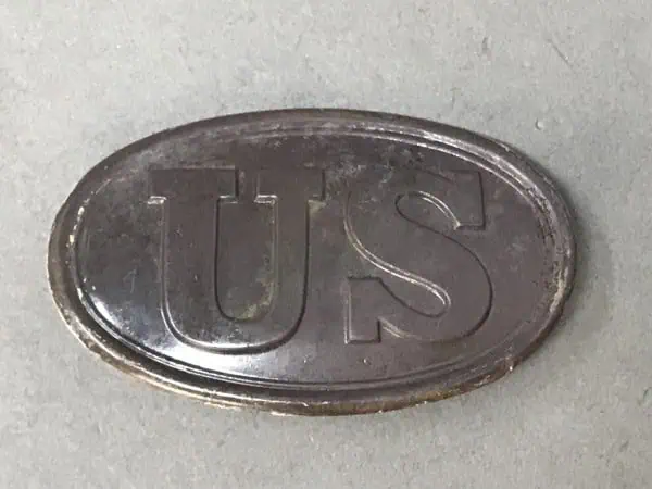 US military badge or insignia with engraved letters "US" on a metallic oval background.