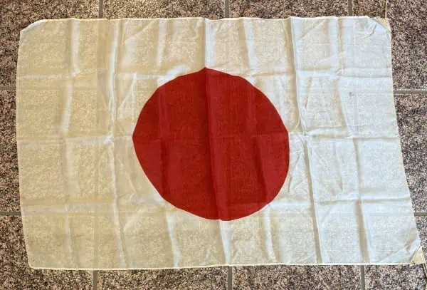 Japanese flag cloth with red circle on white background, laid on tiled surface.