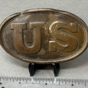 U.S. military badge with embossed letters "US" on a metal oval background.